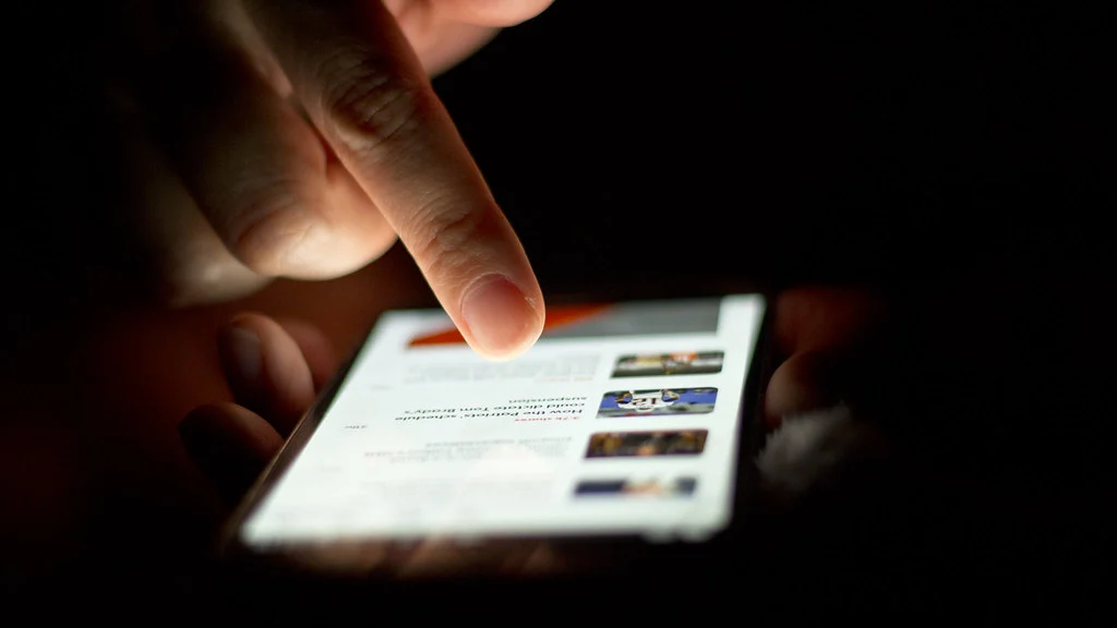 Main faisant défiler l’écran d’un smartphone dans la pénombre